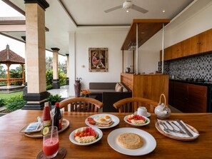 Un comedor con una mesa dispuesta para el desayuno, que incluye platos de comida, una bebida y cubiertos.