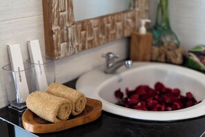 A bathroom with a sink, a wooden tray with towels, and a bowl of rose petals. - Griya Private Villa (Ubud)