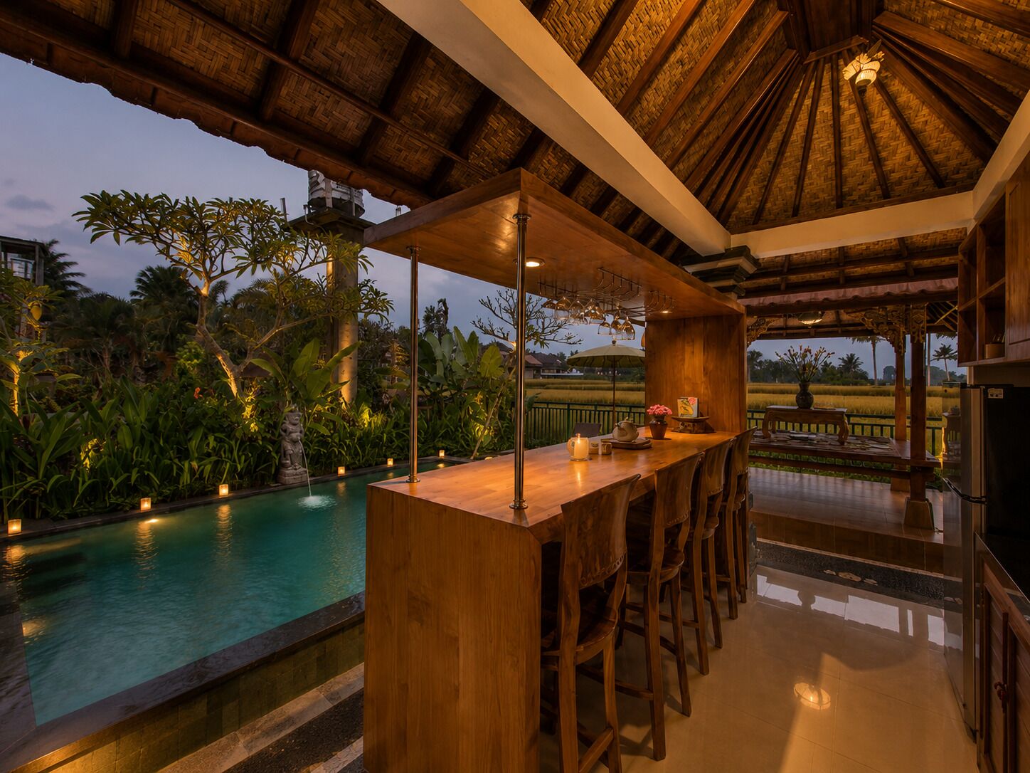 Zona de bar con vistas a la piscina, muebles de madera y techo de paja.