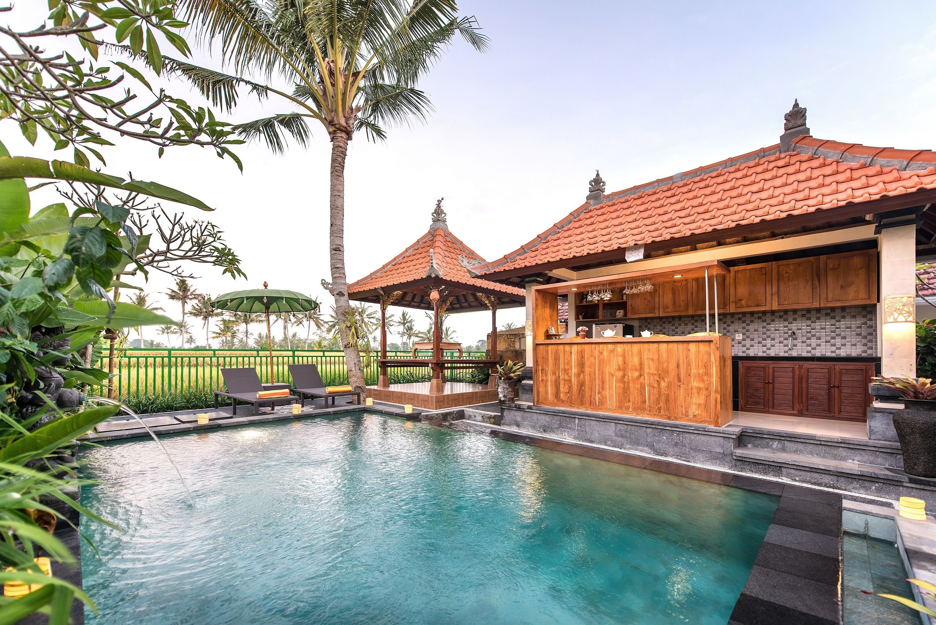 A swimming pool with lounge chairs, a wooden bar, and a tiled roof structure.