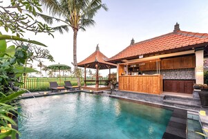 Piscina com espreguiçadeiras, um bar de madeira e uma estrutura de telhado telado.