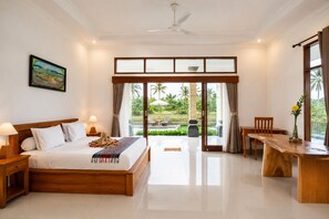 Habitación de hotel con una cama grande, un comedor y vistas a un jardín tropical.