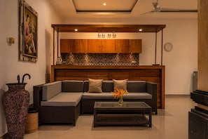 A modern living room with a sofa, a coffee table, a decorative vase, and a kitchen area with wooden cabinets and a tiled backsplash. - Griya Private Villa (Ubud)
