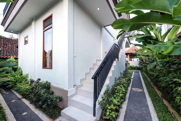 A white building with a staircase leading to a second floor, surrounded by lush greenery and a pathway. - Griya Private Villa (Ubud)