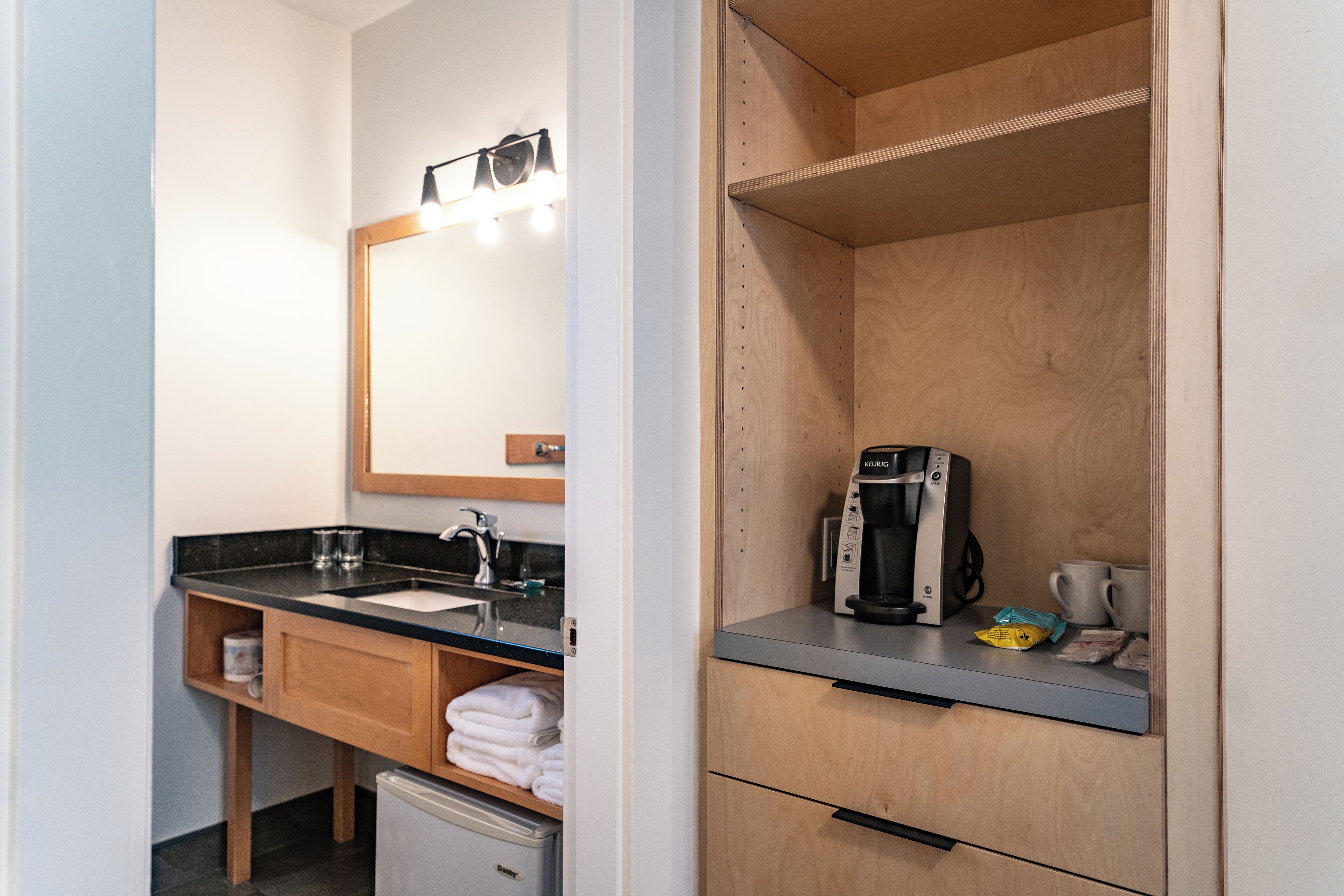 Un baño moderno con lavamanos, espejo y cafetera.