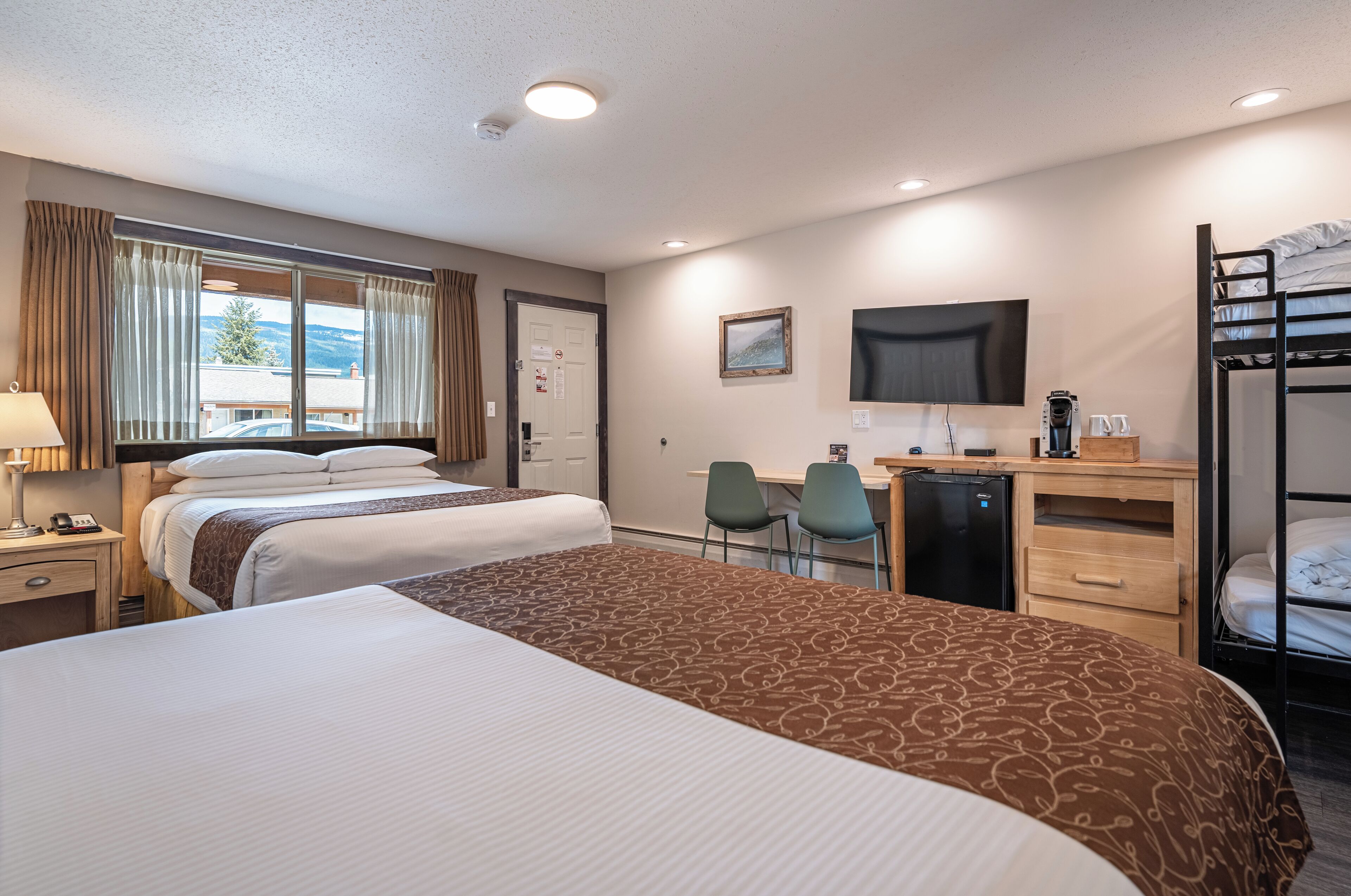 A hotel room with two beds, a desk, a chair, a TV, and a bunk bed.