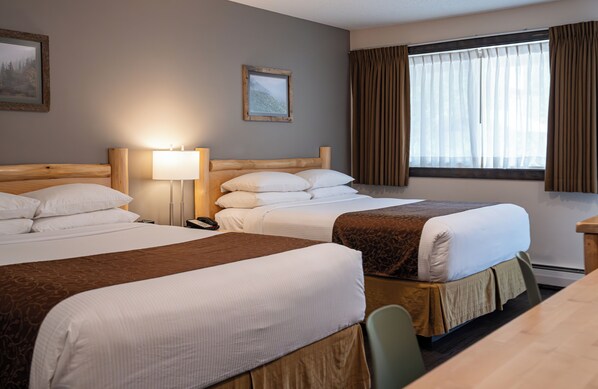 Une chambre d’hôtel avec deux lits, un bureau, une lampe et une fenêtre avec des rideaux.