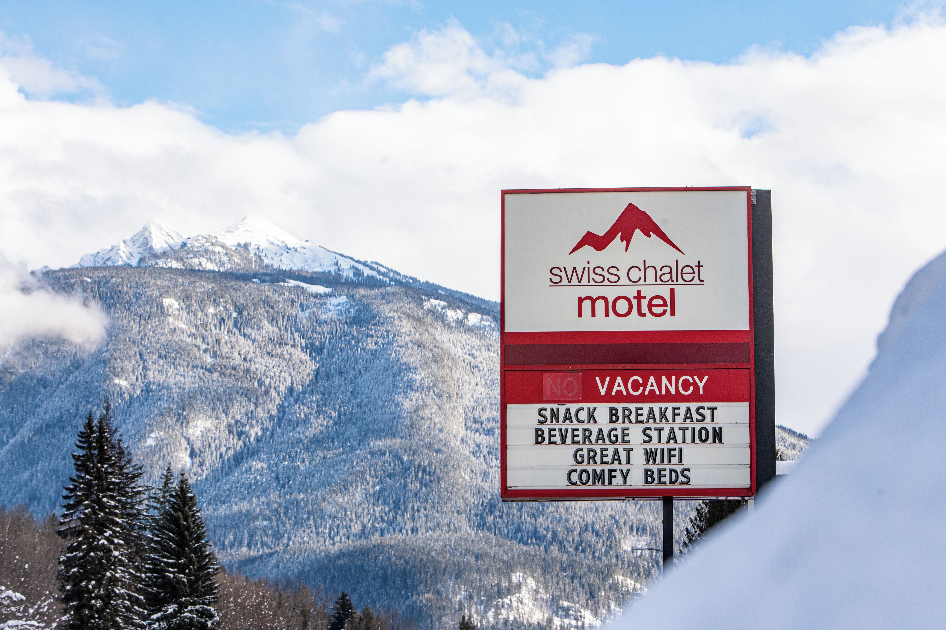Señal del motel Swiss Chalet anunciando disponibilidad, con servicios que incluyen desayuno ligero, estación de bebidas, excelente wifi y camas cómodas.