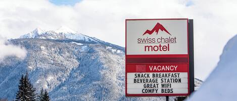Señal del motel Swiss Chalet anunciando disponibilidad, con servicios que incluyen desayuno ligero, estación de bebidas, excelente wifi y camas cómodas.