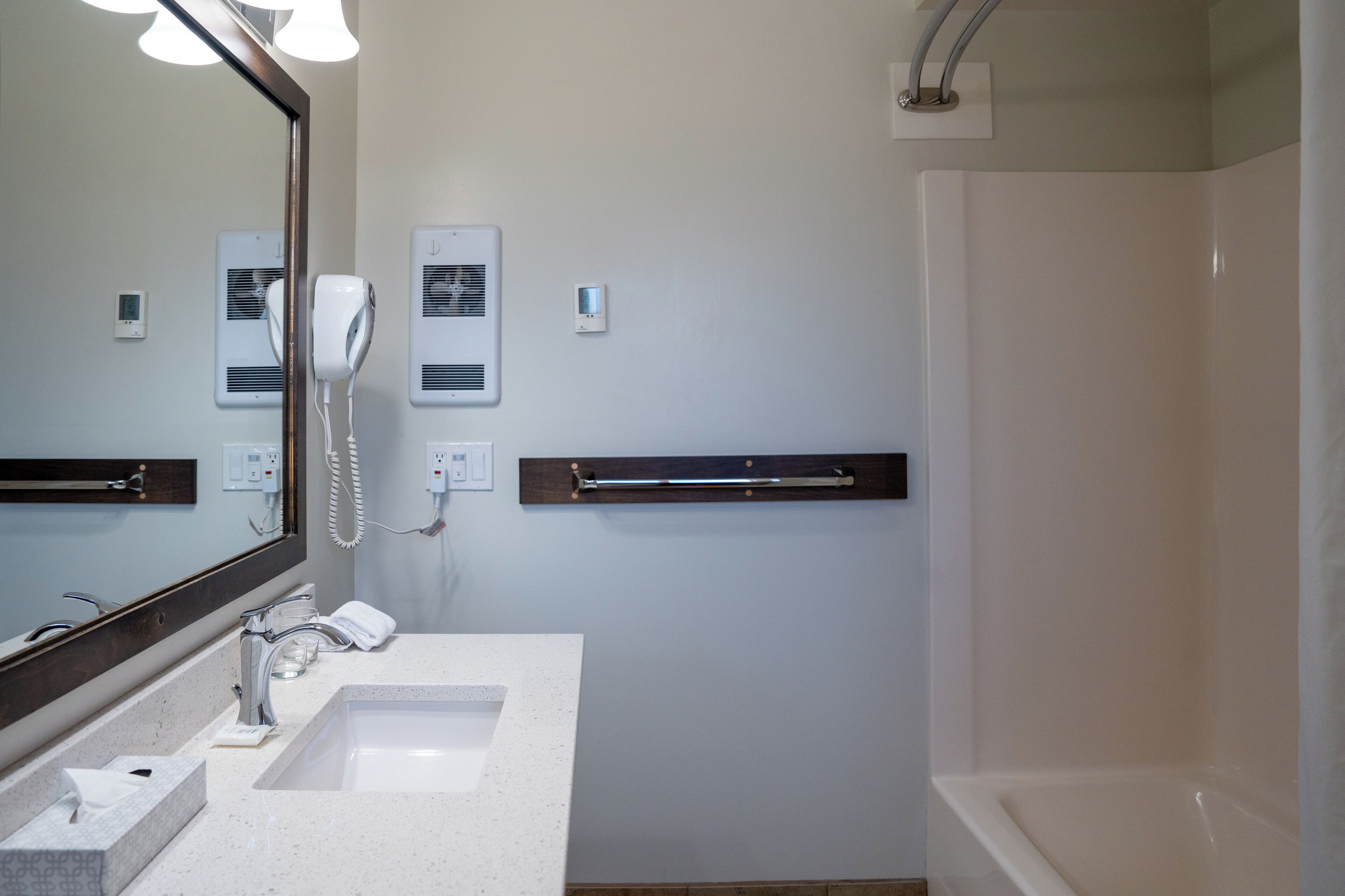 Un baño moderno con un espejo grande, dos lavamanos, un secador de pelo y una ducha.