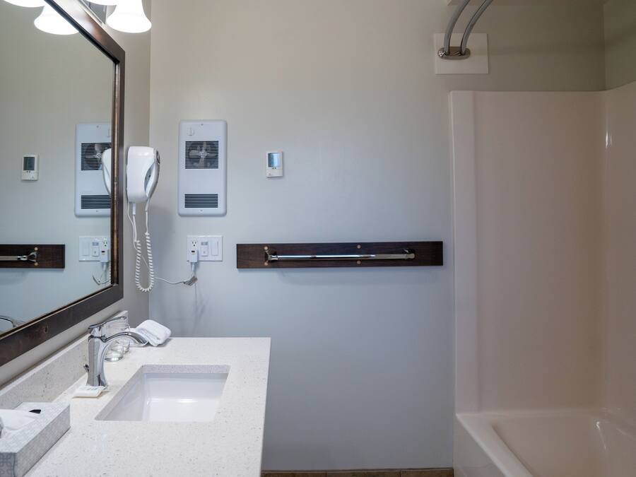 A modern bathroom with a large mirror, two sinks, a hairdryer, and a shower.