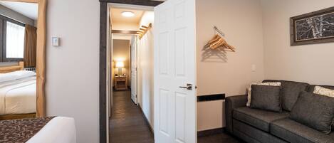 A hotel room with a bed, a sofa, a hallway, and a door leading to another room.