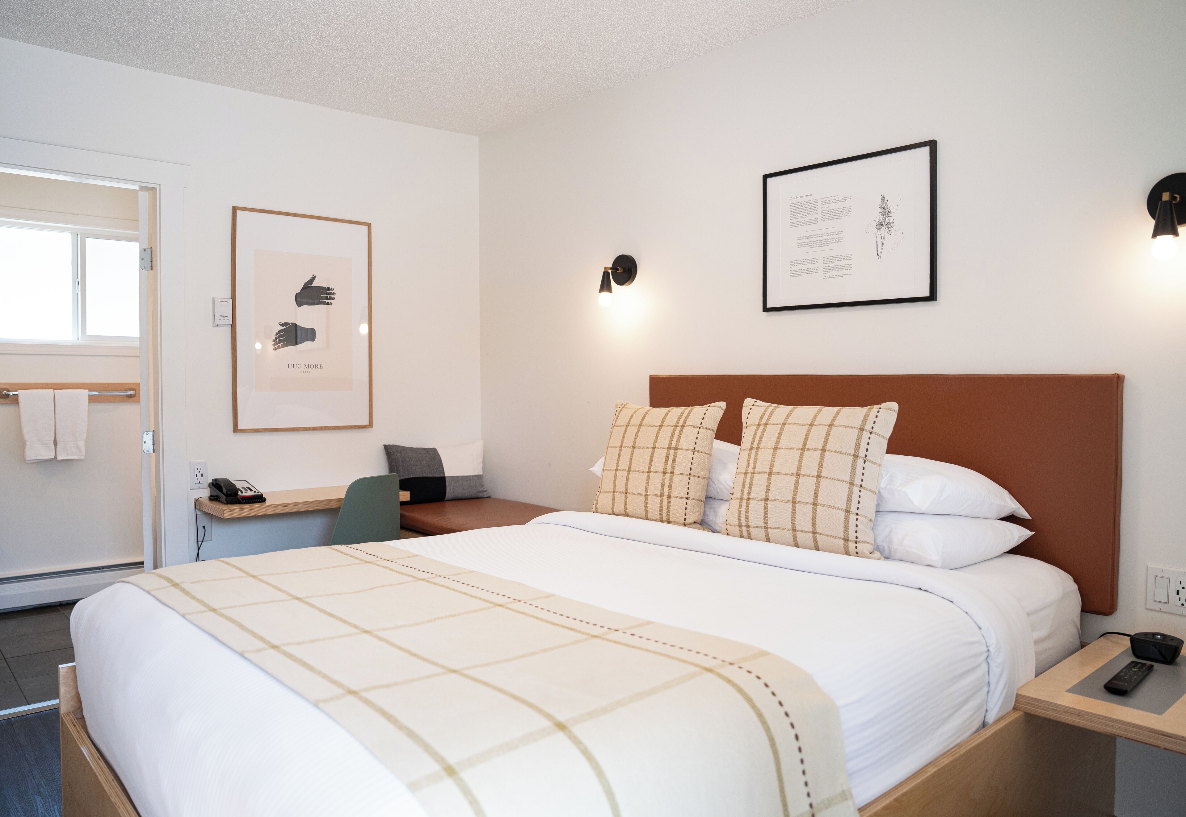 Un cuarto de hotel ordenado con cama, mesita de noche, escritorio y silla.