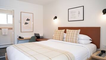Un cuarto de hotel ordenado con cama, mesita de noche, escritorio y silla.