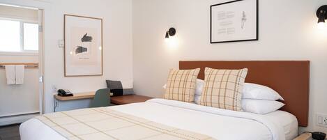 A neatly arranged hotel room with a bed, bedside table, desk, and chair.