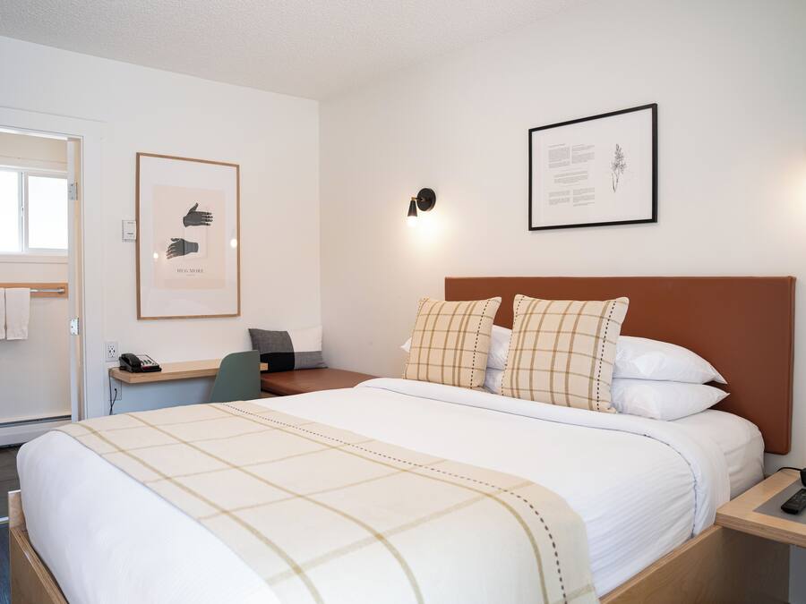 Un cuarto de hotel ordenado con cama, mesita de noche, escritorio y silla.