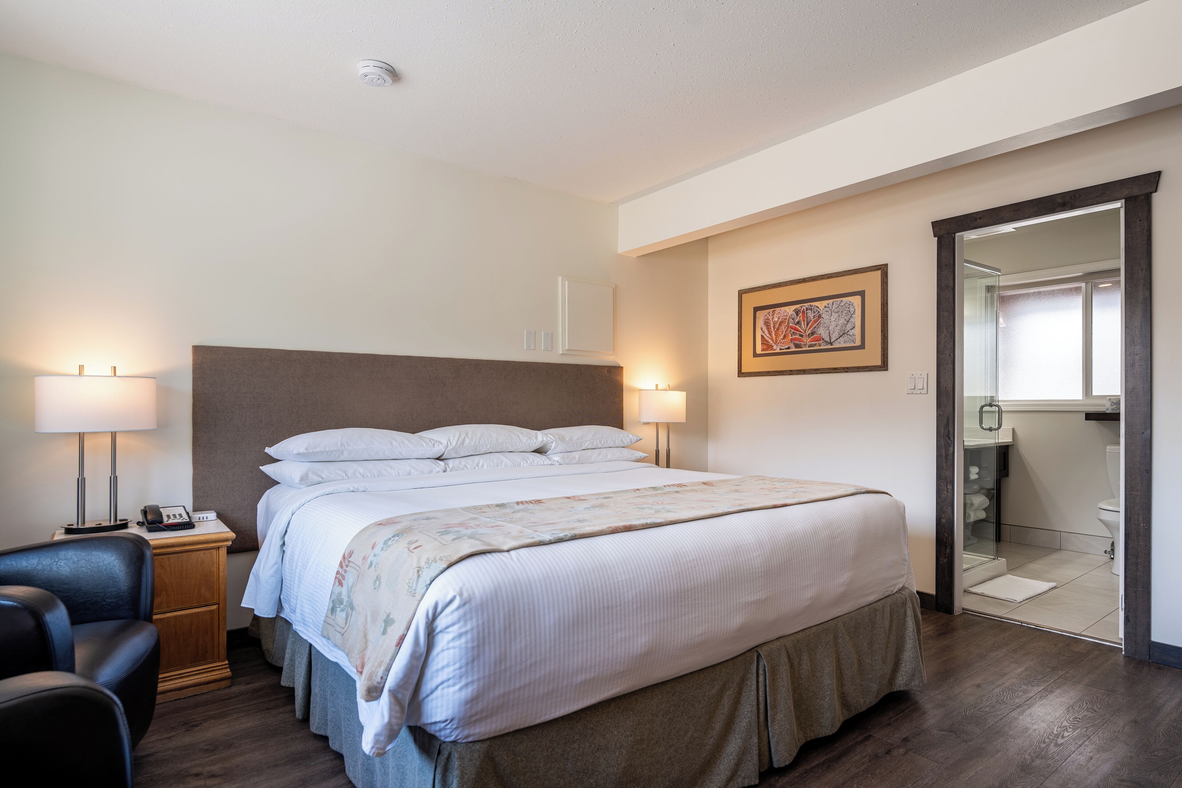 A hotel room with a large bed, bedside lamps, a chair, and a bathroom visible through an open door.