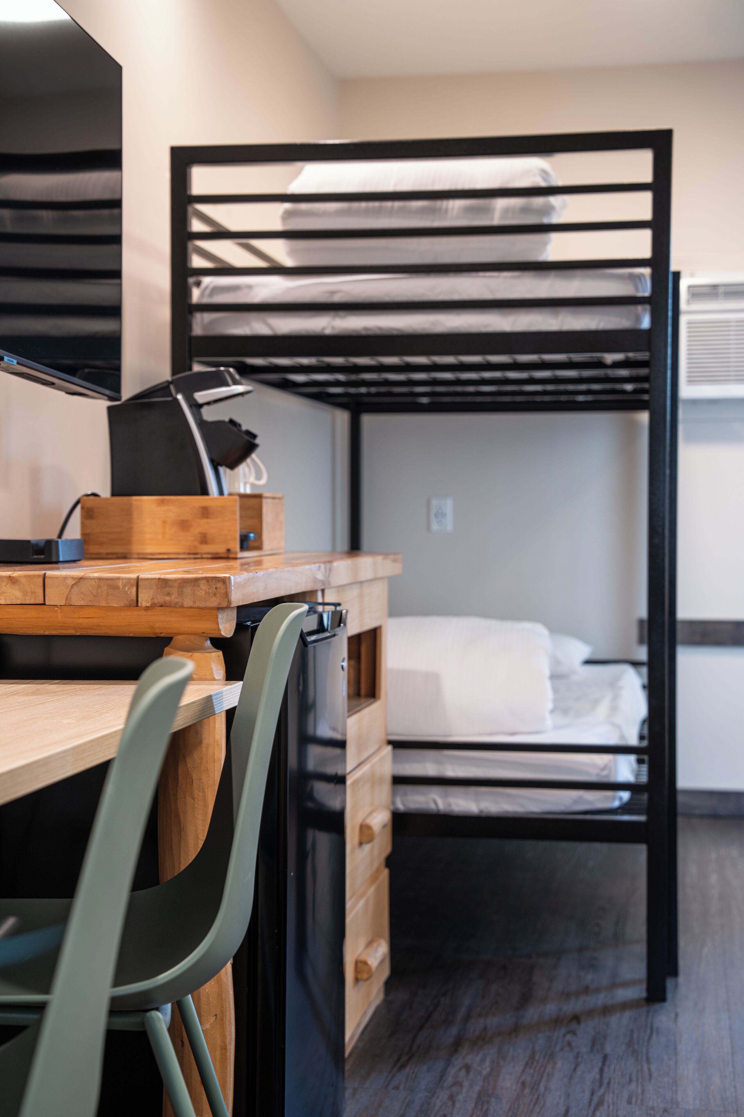 Una cama literera con escritorio y silla, un aparador de madera y una cama con marco negro.
