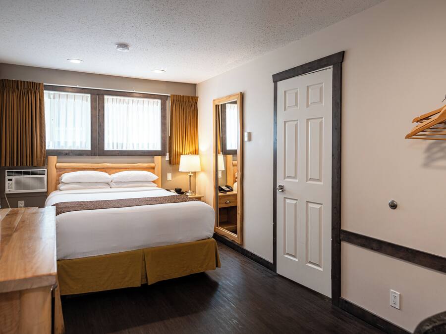 Quarto de hotel com cama, mesa de cabeceira, abajur, espelho e um cabideiro.