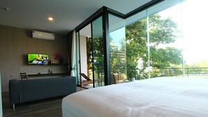 A modern hotel room with a large bed, a seating area, a TV, and a balcony with a view of trees. - Matina Mountain Resort (Koh Tao)