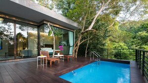 A modern outdoor pool area with a wooden deck, glass walls, and a view of the surrounding forest. - Matina Mountain Resort (Koh Tao)