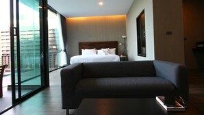 A modern hotel room with a large bed, a dark sofa, a small table, and a glass partition. - Matina Mountain Resort (Koh Tao)