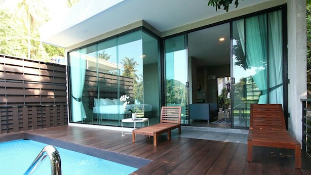 A modern outdoor pool area with wooden decking, a lounge chair, and a glass-enclosed patio. - Matina Mountain Resort (Koh Tao)