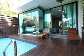 Un área de piscina moderna al aire libre con cubierta de madera, una tumbona y un patio con paredes de vidrio.