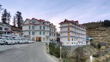 A multi-story hotel with a red roof, white walls, and a parking lot with several cars.