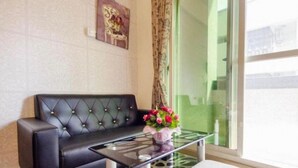 Un sofá de cuero negro con respaldo capitonado, una mesa de centro de vidrio y un jarrón con flores.