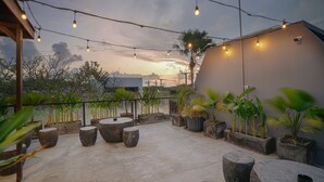 An outdoor patio area with string lights, potted plants, and a view of the sunset. - BRAW inn Canggu (Tibubeneng)