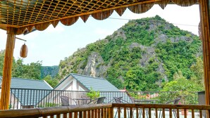 A view from a balcony with bamboo railings overlooking a body of water and a mountain. - Tamcoc Golden Rice (Nam Hoa Lu)