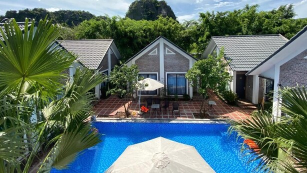 A swimming pool with a patio area, surrounded by houses with tiled roofs and a view of a forested hill. - Tamcoc Golden Rice (Nam Hoa Lu)
