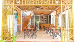 An open-plan restaurant with bamboo partitions, multiple dining tables and chairs, and a staircase leading to an upper level. - Tamcoc Golden Rice (Nam Hoa Lu)