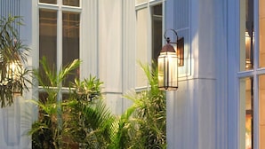 An outdoor seating area with tables and chairs, surrounded by potted plants and a building with large windows. - Kanvaz Village Resort Seminyak (Keroboken Kelod)