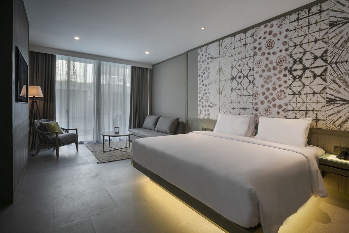 A modern hotel room with a large bed, a sofa, a small table, and a wall with a geometric pattern.