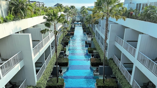A modern hotel with a central swimming pool flanked by palm trees and balconies. - Kanvaz Village Resort Seminyak (Keroboken Kelod)