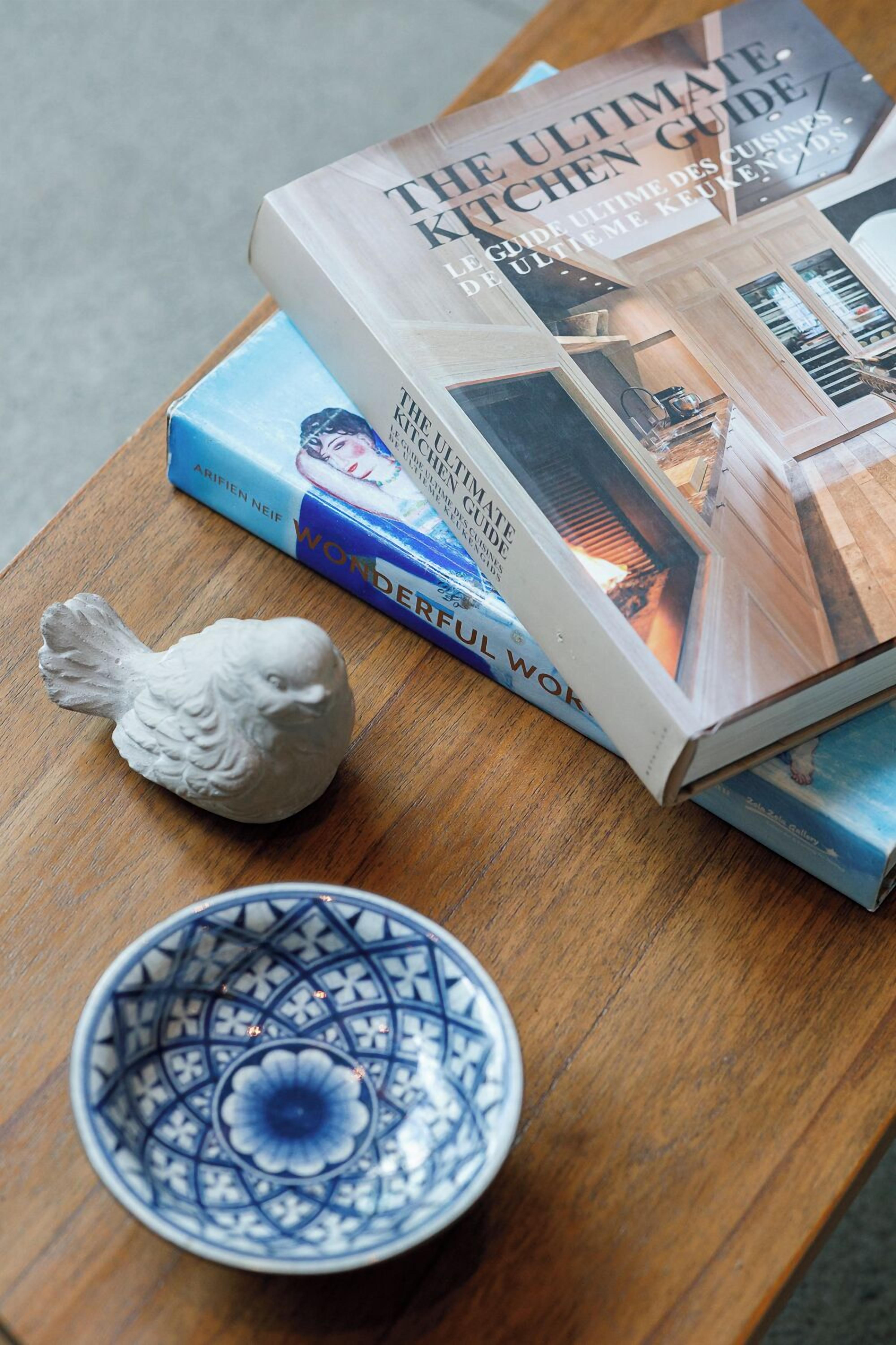 A book titled "The Ultimate Kitchen Guide" on a wooden table, next to a decorative fish and a blue patterned bowl.