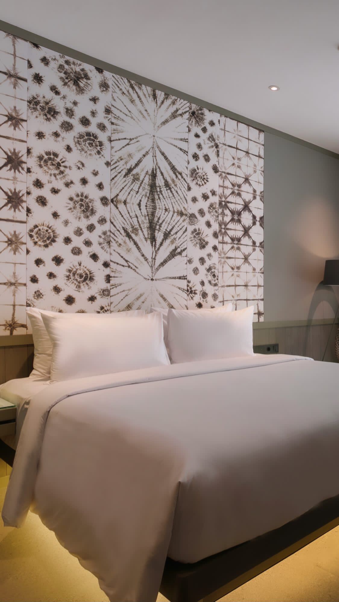 Habitación de hotel con una cama grande, dos almohadas, una mesita de noche y una pared con un diseño geométrico.