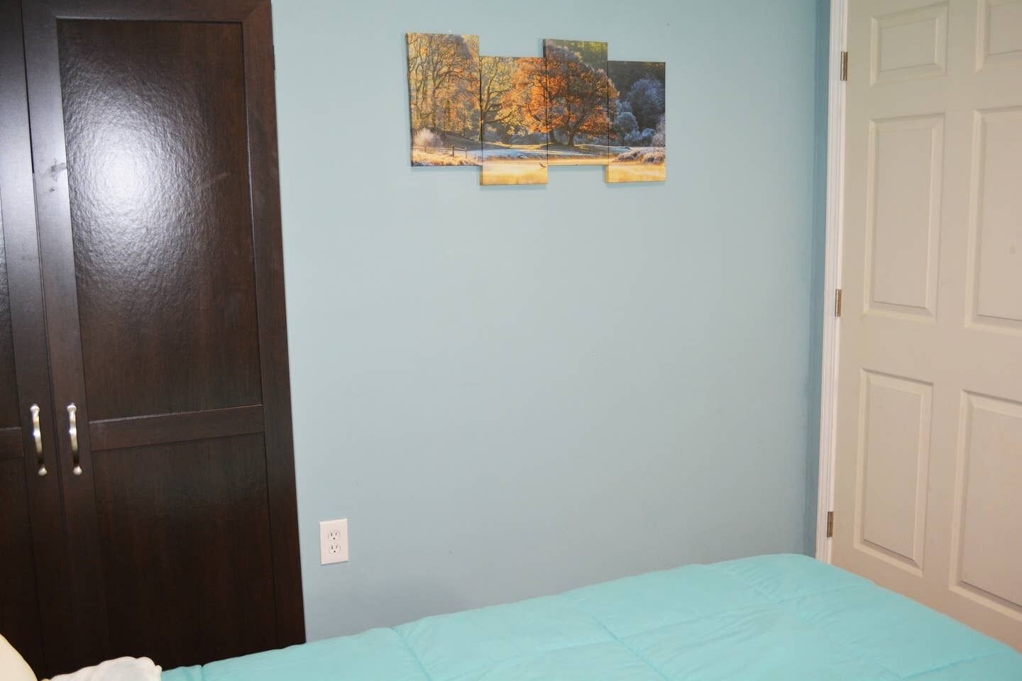 A bedroom with a bed, a dark wooden wardrobe, and a light blue wall.