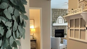 A hallway leading to a living room with a fireplace, a door with a keypad lock, and a plant.