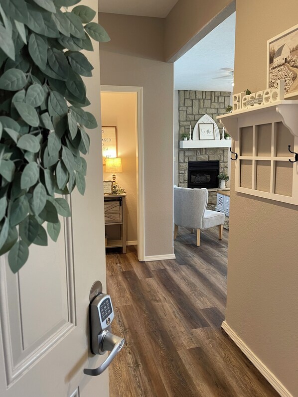 A hallway leading to a living room with a fireplace, a door with a keypad lock, and a plant.