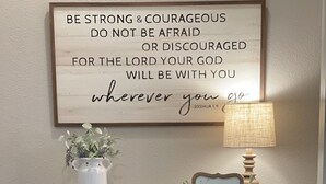 A wooden console table with a motivational quote, a welcome sign, a vase with plants, and a lamp.