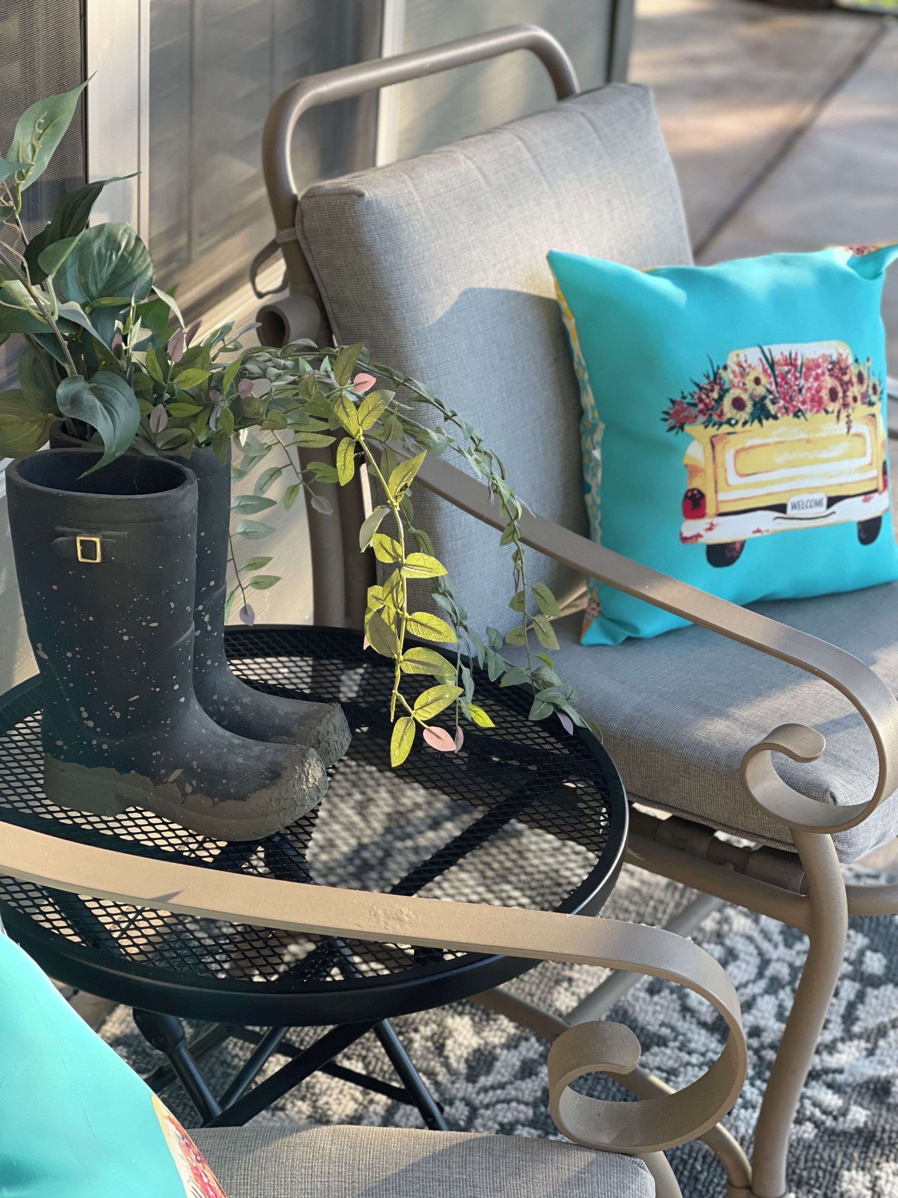 A patio area with a round metal table, a potted plant, a chair with a cushion, and a decorative pillow.