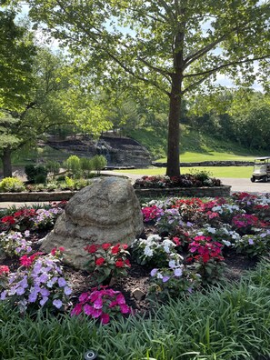 A landscaped garden with a large rock centerpiece, flowering plants, and a view of a golf course in the background.