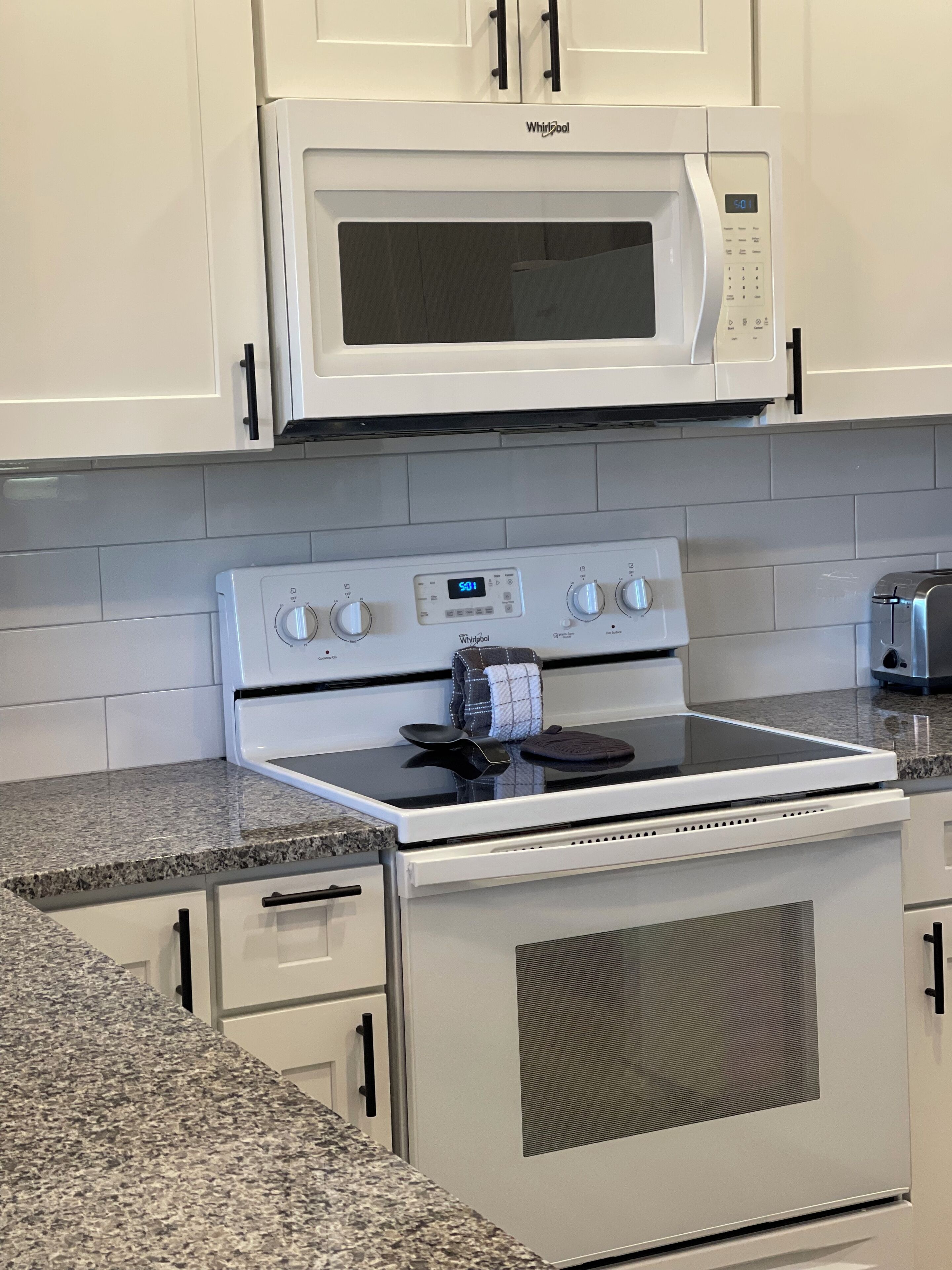A kitchen with white cabinetry, a built-in microwave, a stove with four burners, and a toaster.