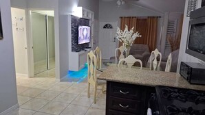 Une cuisine moderne dotée d’un plan de travail en granit, d’un four à micro-ondes encastré et d’une cuisinière. On y trouve également un coin repas avec une table et des chaises en verre, ainsi qu’un téléviseur fixé au mur.