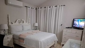 Une chambre à coucher comprenant un lit, des tables de chevet, une commode, un téléviseur et une table basse en verre.