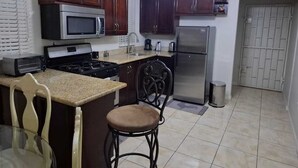Une cuisine avec des meubles de rangement en bois foncé, un réfrigérateur en acier inoxydable, un four à micro-ondes, une cuisinière et un évier. On y trouve un tabouret de bar et une chaise près du comptoir.