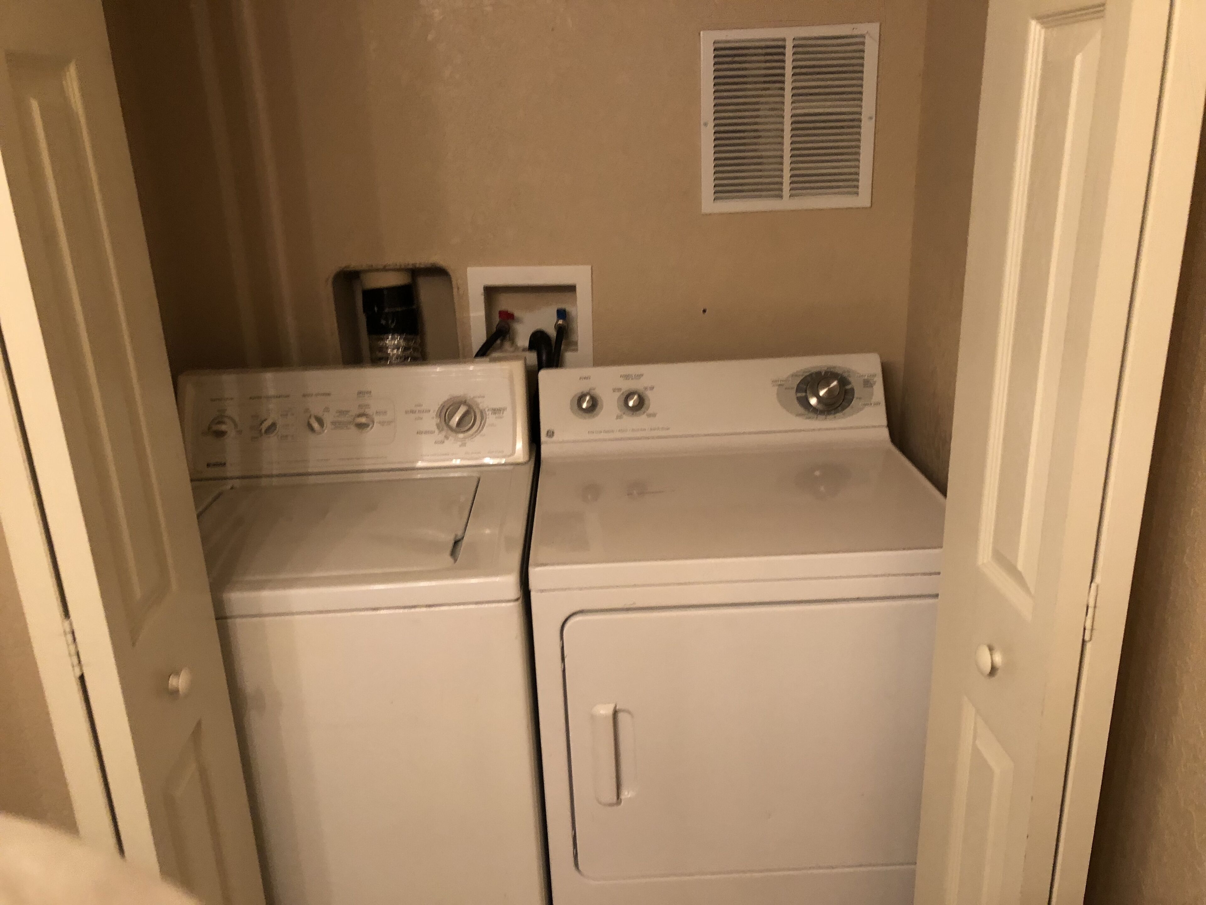 A laundry room with two stacked washers and dryers, a vent, and a coffee maker on the wall.
